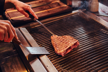 Close-up image of a cooking delicious meat steak on a grill in a restaurant kitchen.