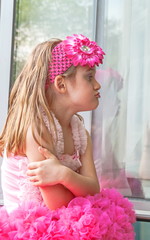pretty little girl in a smart dress is sitting on the windowsill and making funny faces
