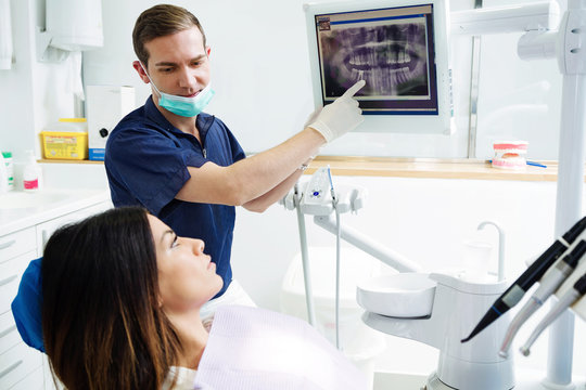 Attractive young dentist showing to his patient radiography of her mouth in the dental clinic.