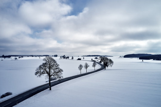 Aerial View Of A Winter Curved Road Covered With Snow. A Snowy Plateau With Single Trees Captured From Above With A Drone.