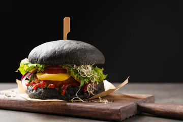 Board with tasty black vegetarian burger on table against dark background
