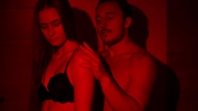 Seductive and sensual man and woman touch each other tender sitting in the bathroom. Shooting in bright red light.