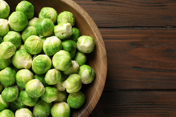 Bowl of fresh Brussels sprouts on wooden background, top view with space for text