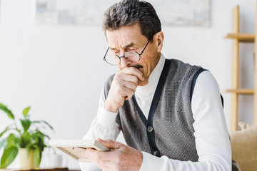retired man in glasses crying while looking at photo at home
