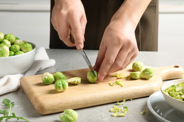 Woman cutting fresh Brussels sprouts on wooden board, closeup - Powered by Adobe