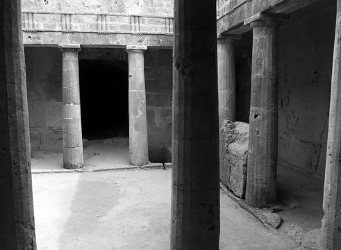 monochrome corner view of an underground chamber at the tombs of the kings in paphos cyprus with old eroded sandstone columns surrounding a dark empty doorway