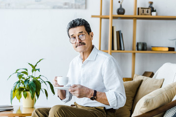 senior man holding cup with coffee while sitting on sofa