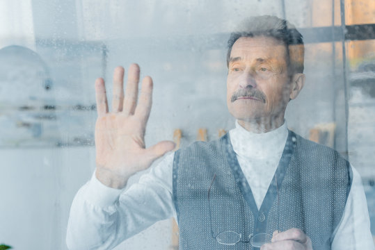 Sad Senior Man Waving Hand While Standing Near Window