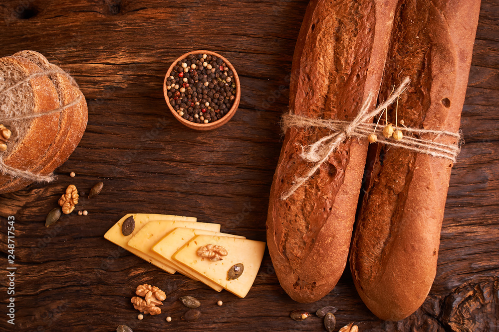 Wall mural Peppercorns in a wooden bowl on table with stack of bread and two baguettes Homemade food