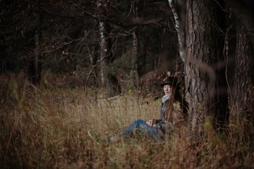 A girl sits alone under a tree in a forest on a sunny day.