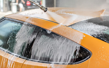 Yellow car washed in self serve carwash, water jet spray cleaning up the shampoo and foam from the...