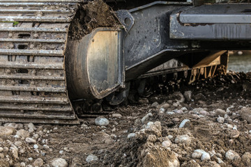 Heavy excavator (digger machine) track detail, some stones in foreground. Abstract industrial / construction background.