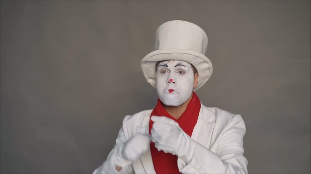 Dangerous mime. Portrait of a joker. Crazy image of a man in a white suit. Mime threatens to camera. The man shows gestures threat.