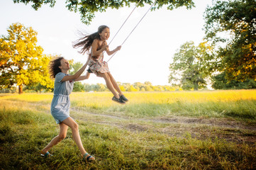 Mom swinging daughter on a swing in the field - obrazy, fototapety, plakaty