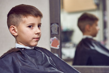 Cheerful Caucasian boy  getting hairstyle in barbershop.