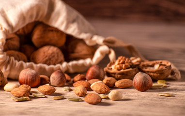 Almond nuts, hazelnuts, walnuts and sweet seeds in a burlap bag on a wooden background.