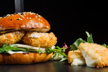 Hamburger with cheese sticks laid out on a black slate. Cheese beautifully flows.