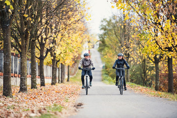 A senior couple with electrobikes cycling outdoors on a road.