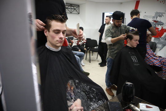 master hairdresser does hairstyle and style with scissors and comb. Master stacks hair of men in barbershop, hairdresser makes hairstyle for young man. Barber shop. Light 