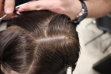 master hairdresser does hairstyle and style with scissors and comb. Master stacks hair of men in barbershop, hairdresser makes hairstyle for young man. Barber shop. Light 