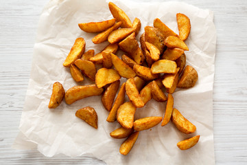 Fried potato wedges on a white wooden background. From above, overhead. Close-up.