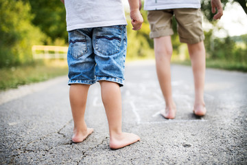 A rear view of two small boys hopscotching on a road in park on a summer day.