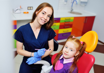 children's dentist examines the teeth and mouth of the child - a cute red-haired girl sitting in a dental chair. Pediatric dentistry