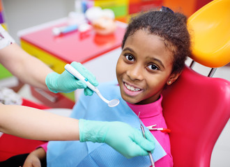 African American baby girl smiling sitting in a dental chair at the examination of the pediatric dentist.