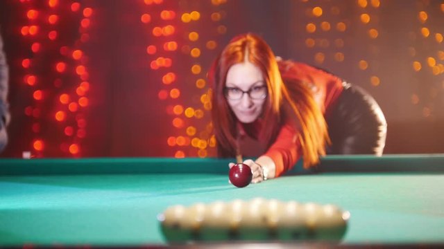 Concentrated ginger woman playing billiard in billiard club. Breaks down arranged balls