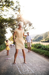 Obraz premium A young family with small children playing hopscotch on a road in summer.