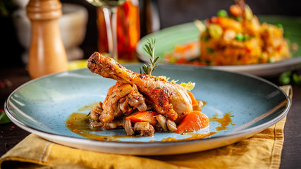 Concept of Italian cuisine. Stewed chicken in strong wine with vegetables. Serving dishes in a restaurant in a blue plate. White wine sherry in a glass on the table. Copy space