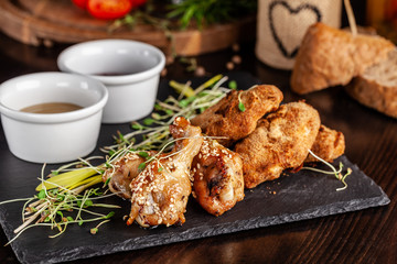 The concept of Italian cuisine. Snack to beer. Glazed chicken legs and chicken wings, breaded. Serving dishes in the restaurant on a black stone slate. Copy space