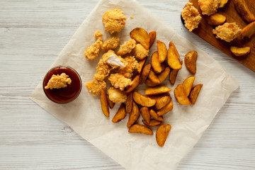 Fastfood: fried potato wedges, chicken bites with barbecue sauce on a white wooden background, top view. Flat lay, overhead.