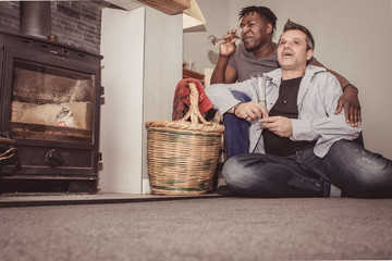 A multi ethnic gay couple sits at home by the fireplace - in Britain - spending a cozy time together. 