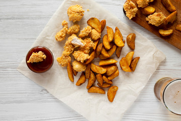 Fastfood: fried potato wedges, chicken bites, barbecue sauce and beer on a white wooden background, top view. Flat lay, overhead.