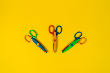 Three colourful scissors on the yellow background. Fancy kids scissors with different cutting...
