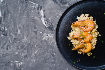 Italian risotto with shrimp on a black plate.. Dark background, top view, space for text