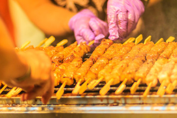 Close up the vendor grilling pork satay, Thai steak roasted pork grilling on the fire screen at night market in Bangkok, Thailand.