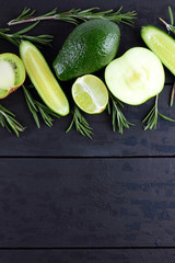 Green fruits, vegetables and rosemary on black boards with copy space. Avocado, lime, kiwi and green apple on wooden boards. Cucumbers and rosemary branches top view. Healthy food