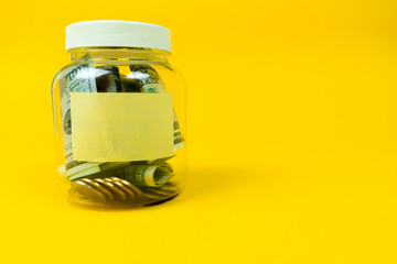 Money jar with coins and paper dollars with sticker for your text, copy space. Isolated on yellow background. Close up