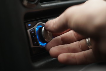 Close-up of man hand adjusts the volume control of car audio system 