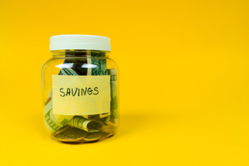 Money jar ful of paper bills and coins with savings sign on the sticker. Isolated on yellow background. Copy space