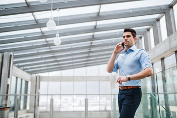 A low-angle view of young businessman with smartphone in corridor outside office.