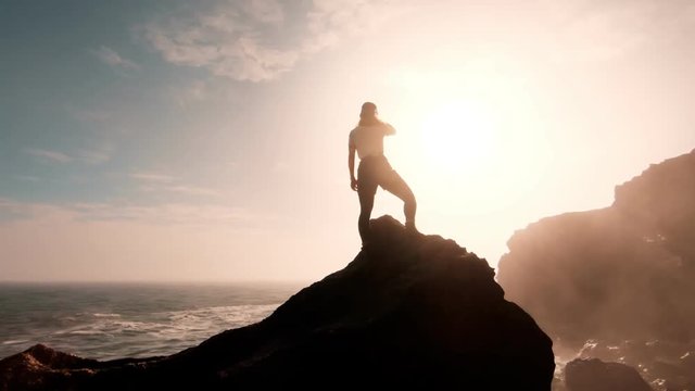 Young adventurous woman, successful and ndependent, confident and empowered female stands on top of rock or mountain looks into sunset horizon over ocean. beautiful accomplishment outdoors lifestyle