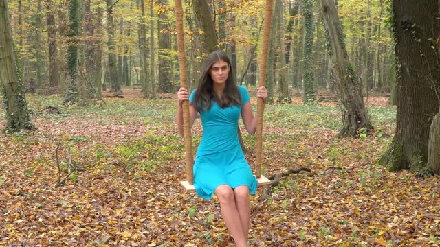Woman with blue dress sitting on a swing at the forest.