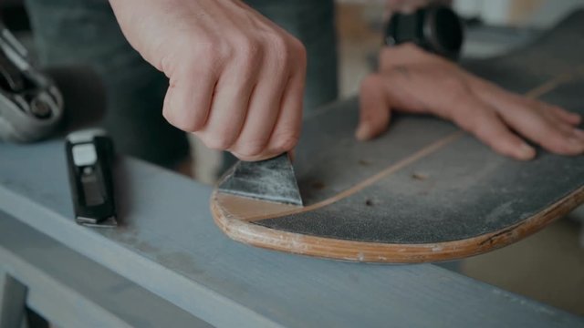 Skateboarder or longboarder prepares his board to new season, regrips tape, replaces it for new adhesive tape. Peels out tape with fingers. Pulls gently. Concept diy at home