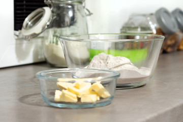 Produkty spożywcze masło i  mąka stoją na kuchennym blacie w szklanych pojemnikach. 