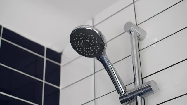 A static close up shot of a chrome shower head stopping, once the pressure of the water stops, it drips and dibbles some left over water. Shower being turned off.