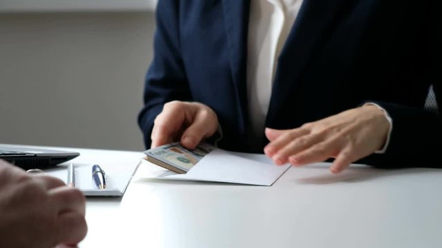 A woman giving bribe money in a white envelope to another businessman in a corruption scam, close up