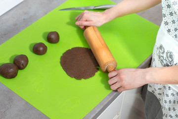Kobiece dłonie wałkują ciasto na wypieki na zielonej silikonowej stolnicy leżącej na kuchennym blacie.